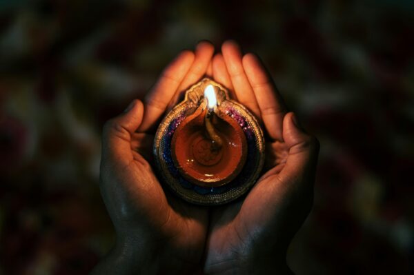 A pair of hands hold an antique oil lamp with lit wick